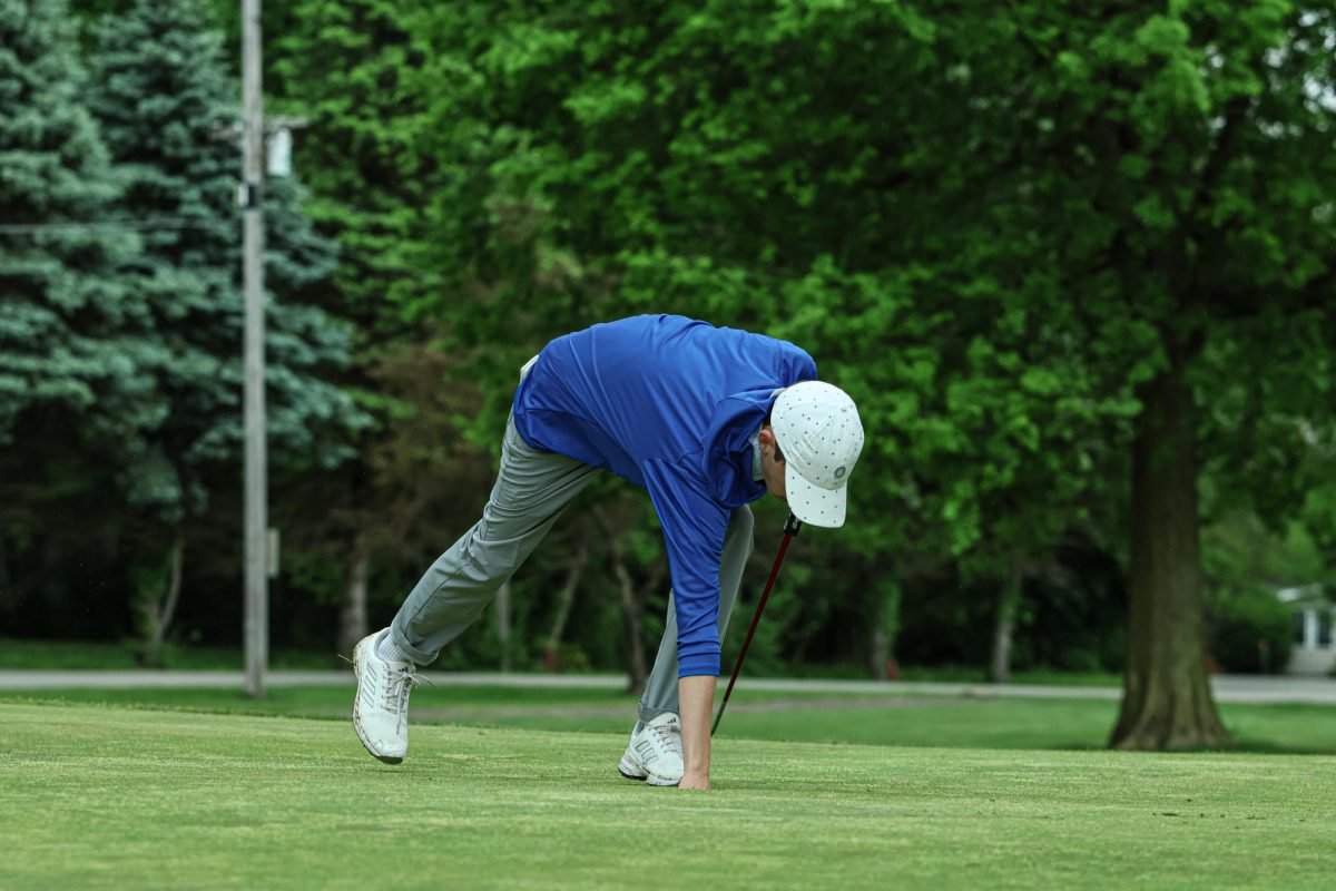 Senior, Aidan Huffer reaches into the hole to pick up his ball at Fall Creek Golf Club on May 9th, 2024